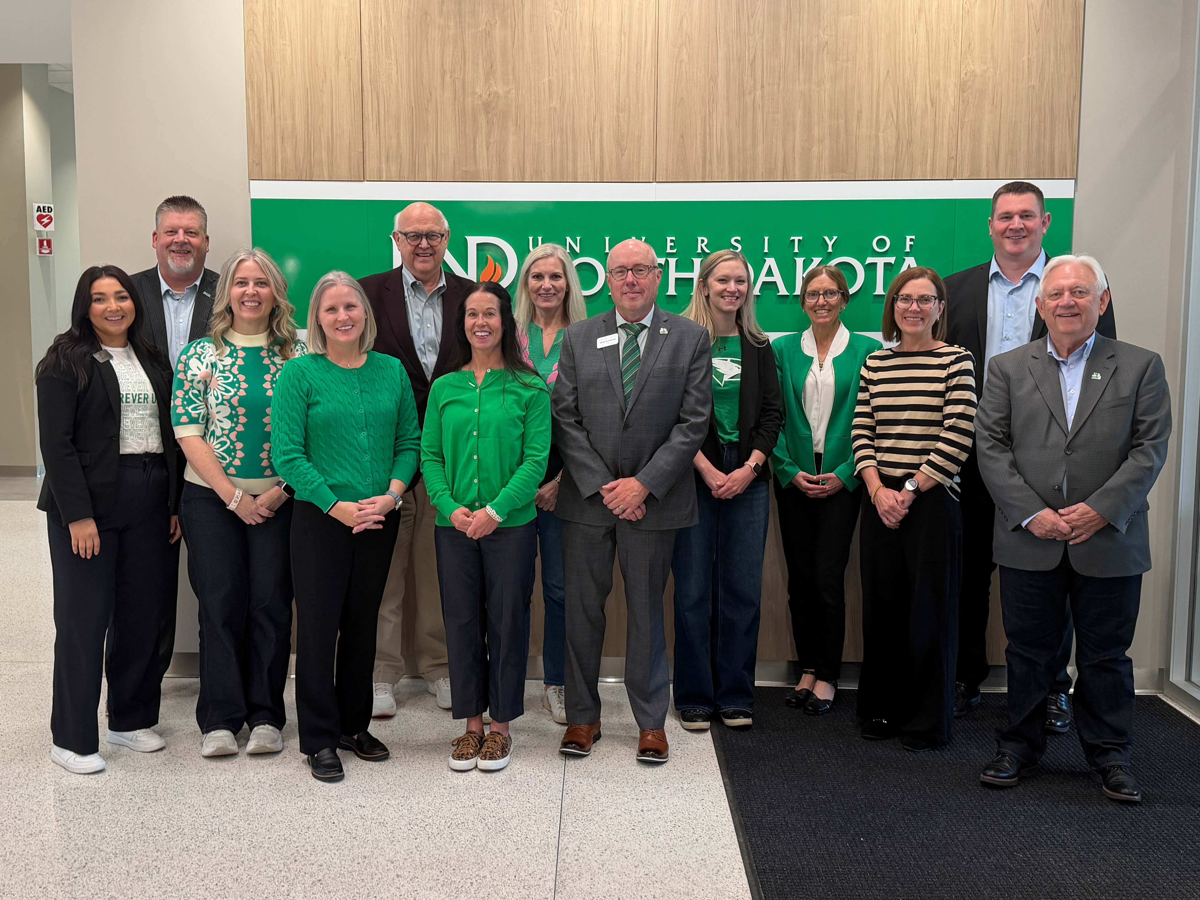Group of advisory board members in front of UND wall signage