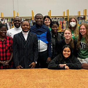 students stand at table in front of bookshelves