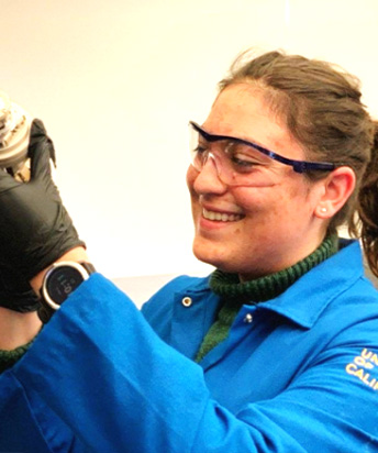 Van Orman in lab coat and goggles holding small equipment