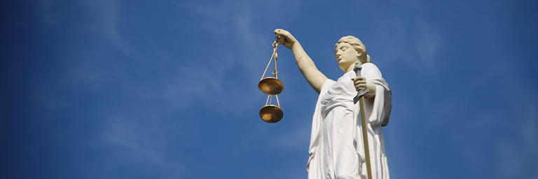 Monument statue holding the scales of justice against a blue sky background