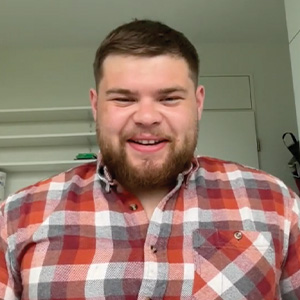Cole Champlain in his white dorm room with a red plaid shirt on