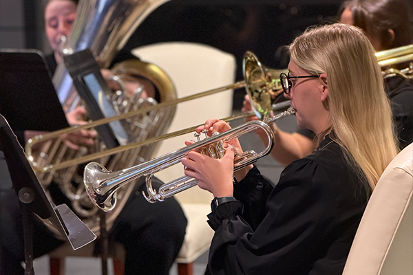 Student playing a silver trumpet in the brass quintet with a trombone player in the background