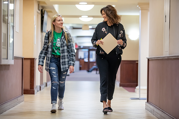 Student walking down Columbia Hall hallway with instructor and notepad