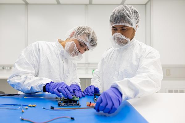 Two studnets working on a computer chip in a cleanroom with full protective gear on.