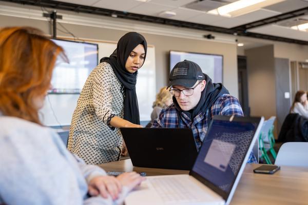 A person helping another one on a laptop.