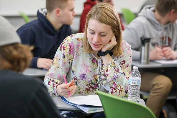 math student looking over notebook sitting at individual desk in classroom