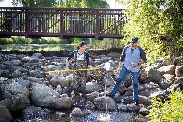 Students in waders sifting in the water of the English Coulee with bridge in background