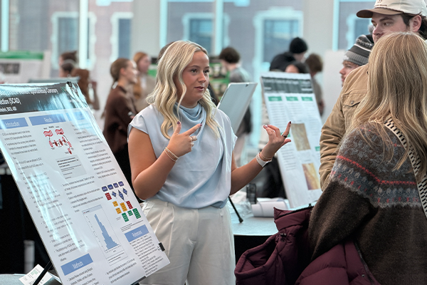 Student speaking with guests next to research posterboard