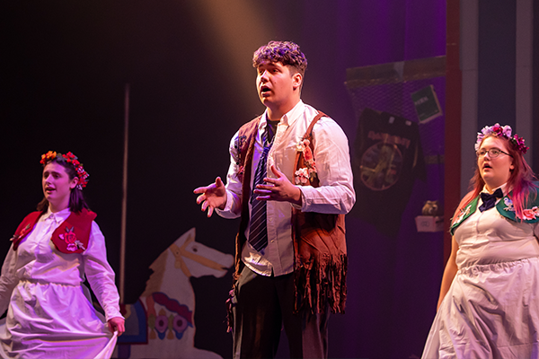 Student speaking in dimmed theatre lights with flanking students all in costume